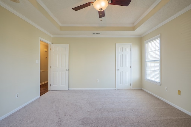 carpeted empty room with ornamental molding, a raised ceiling, and baseboards