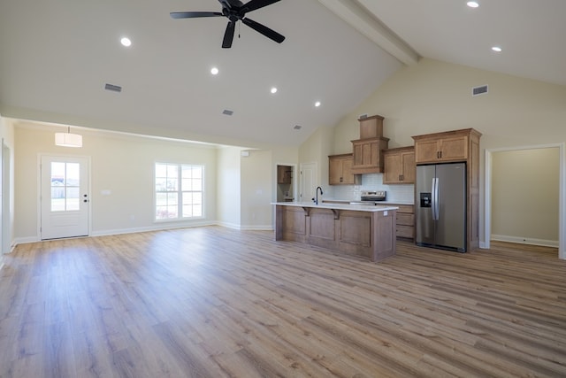 kitchen featuring visible vents, a kitchen breakfast bar, open floor plan, appliances with stainless steel finishes, and brown cabinetry