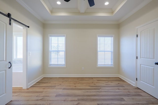 spare room with crown molding, light wood finished floors, a barn door, a ceiling fan, and baseboards