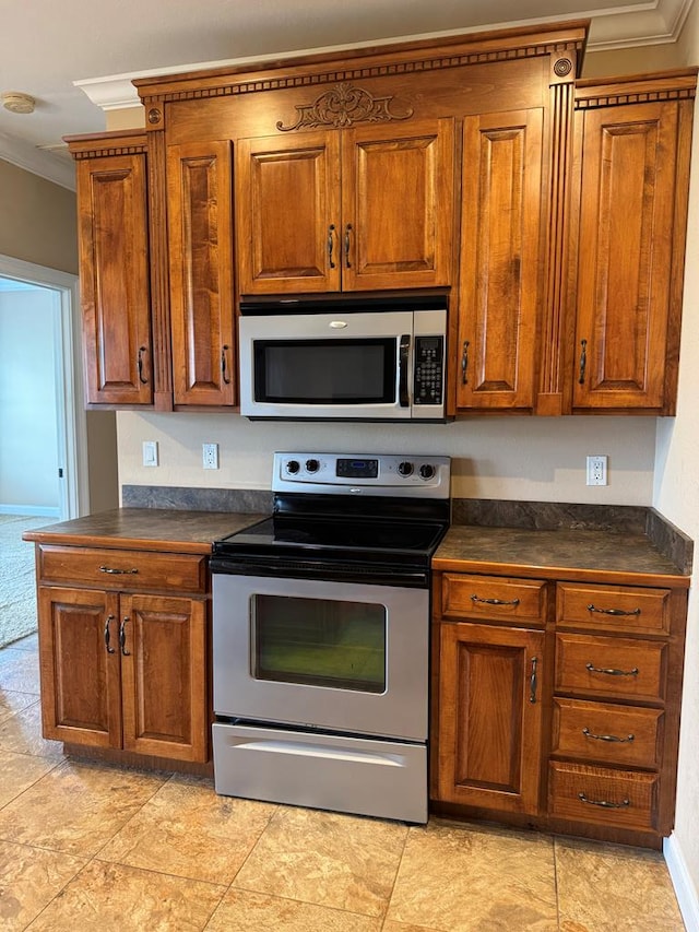 kitchen featuring stainless steel appliances, dark countertops, ornamental molding, and brown cabinetry