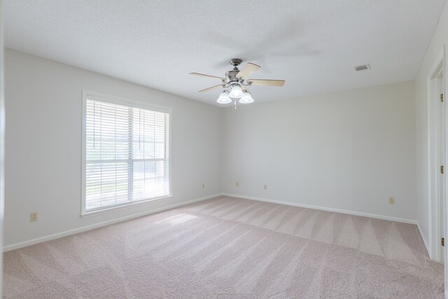 unfurnished room with a textured ceiling, visible vents, ceiling fan, and light colored carpet