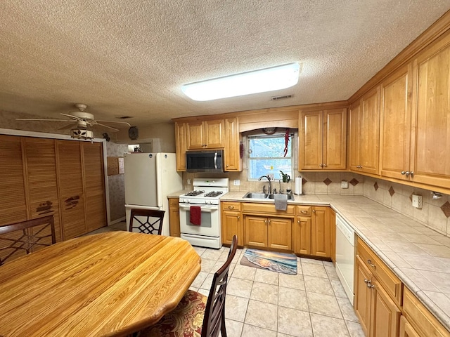 kitchen featuring sink, decorative backsplash, tile counters, ceiling fan, and white appliances