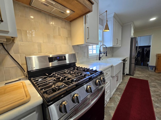 kitchen with washer and clothes dryer, custom exhaust hood, stainless steel appliances, light countertops, and white cabinetry