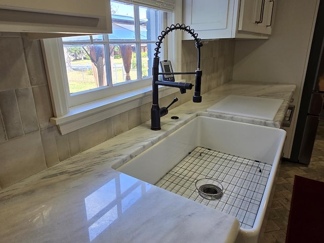 room details featuring refrigerator, white cabinets, a sink, and light stone countertops