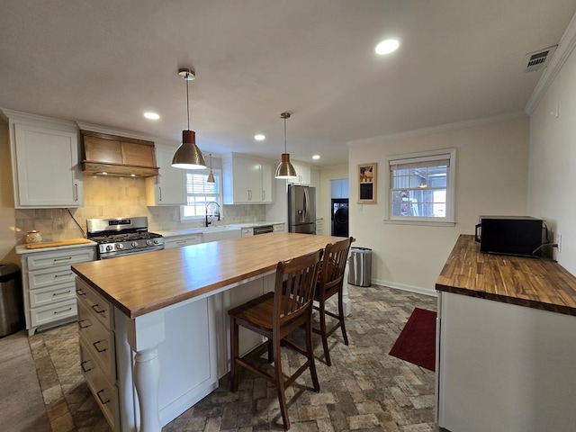 kitchen with visible vents, custom range hood, appliances with stainless steel finishes, a sink, and butcher block countertops