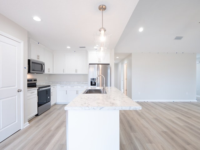 kitchen with stainless steel appliances, a sink, light wood-style floors, light countertops, and a center island with sink