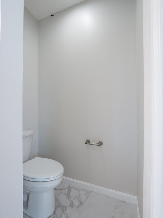 bathroom featuring marble finish floors, toilet, and baseboards
