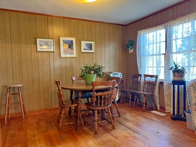 dining room with wood walls, wood-type flooring, and ornamental molding