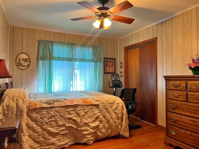 bedroom featuring wood walls, ceiling fan, ornamental molding, wood-type flooring, and a closet