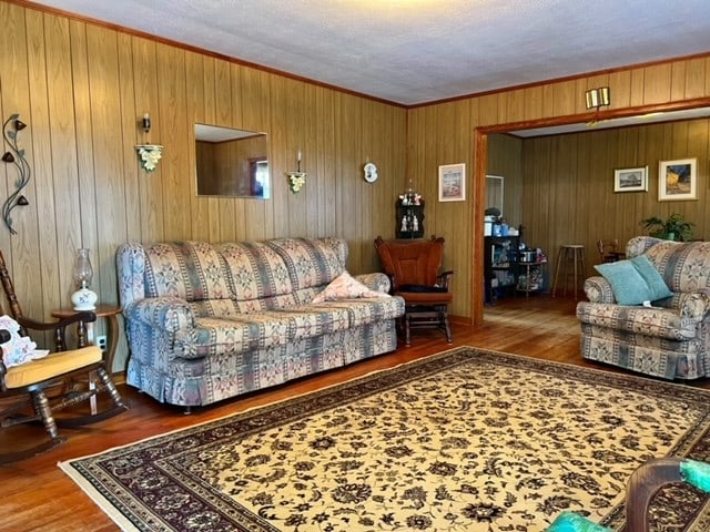 living room with hardwood / wood-style floors, wood walls, ornamental molding, and a textured ceiling