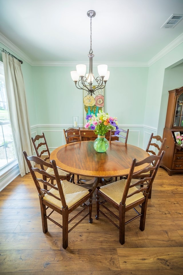 dining area featuring a chandelier, visible vents, ornamental molding, and wood finished floors