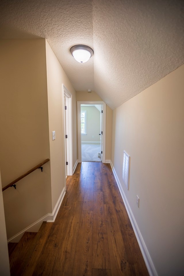 hallway with baseboards, wood-type flooring, and a textured ceiling