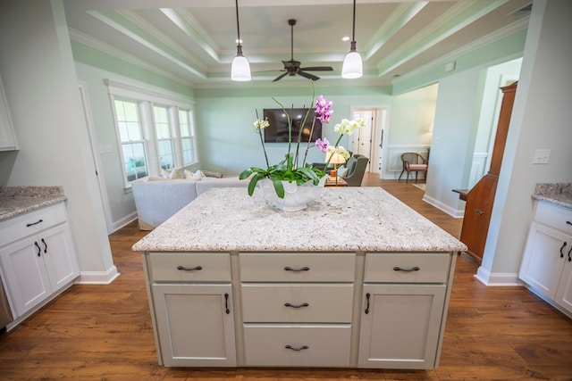 kitchen featuring dark wood-type flooring, ornamental molding, a tray ceiling, open floor plan, and hanging light fixtures