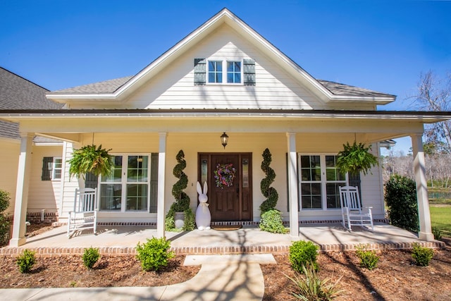 entrance to property featuring covered porch and roof with shingles