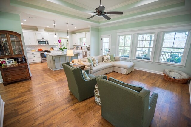 living area featuring visible vents, crown molding, hardwood / wood-style flooring, a raised ceiling, and a ceiling fan