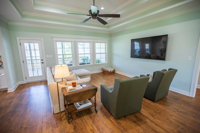 living room featuring a raised ceiling, crown molding, wood finished floors, and baseboards