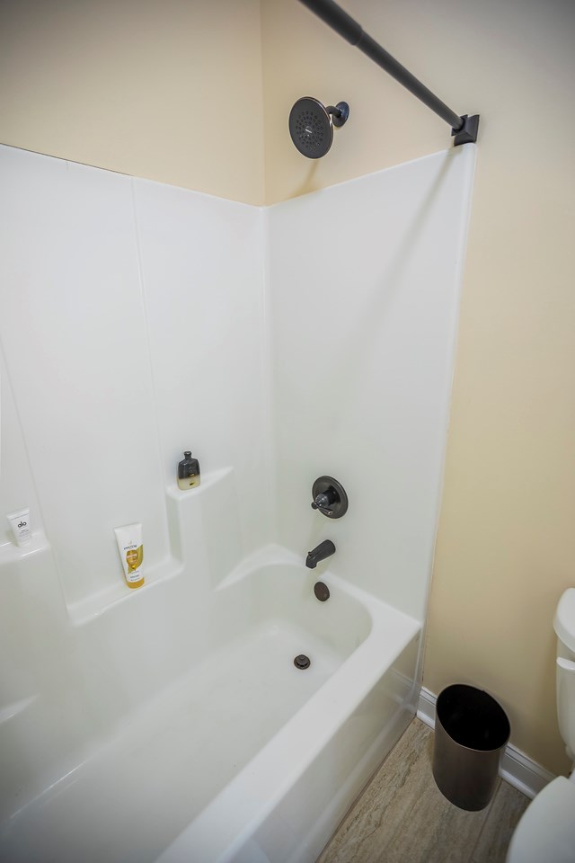 full bath featuring toilet, wood finished floors, baseboards, and shower / washtub combination