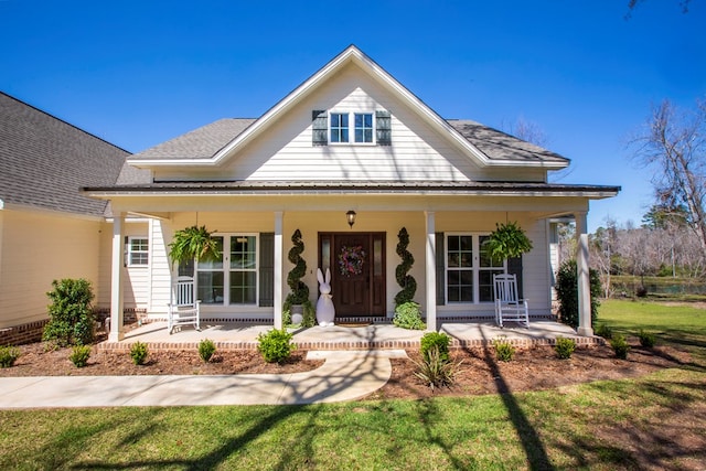 view of front facade with roof with shingles, covered porch, and a front yard