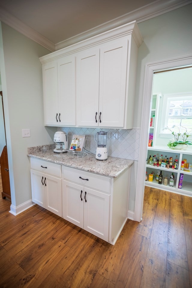 bar featuring decorative backsplash, dark wood-type flooring, baseboards, and ornamental molding