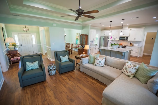 living room with dark wood finished floors, visible vents, crown molding, and a raised ceiling