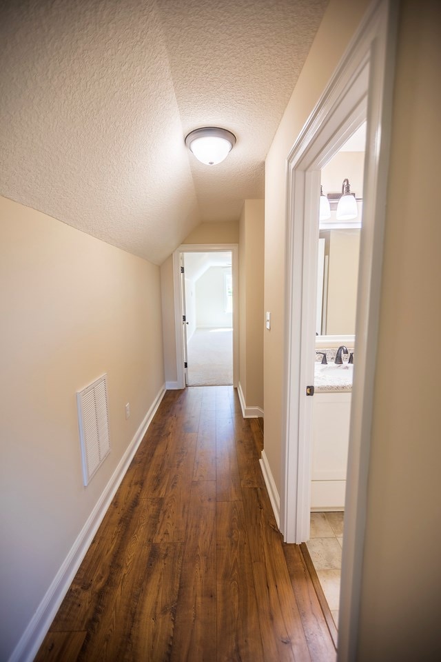 hallway with visible vents, baseboards, lofted ceiling, a textured ceiling, and dark wood-style flooring