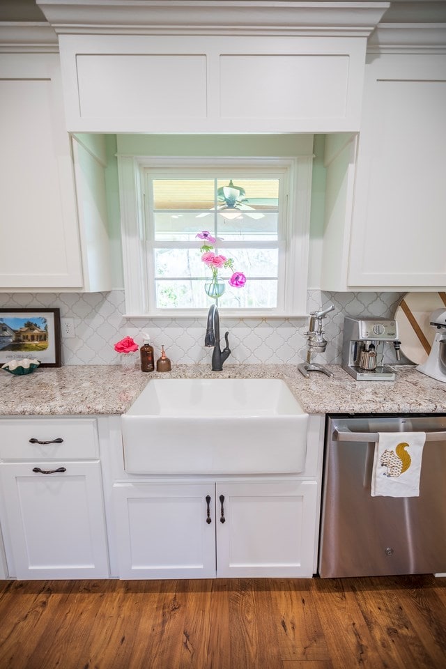 kitchen with light stone counters, white cabinetry, a sink, dishwasher, and backsplash