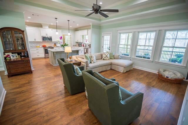 living room featuring crown molding, a ceiling fan, dark wood-type flooring, and a tray ceiling