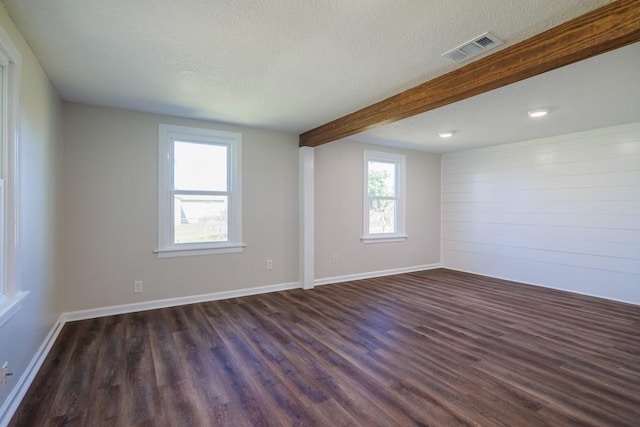 spare room featuring beamed ceiling, a textured ceiling, dark hardwood / wood-style floors, and a wealth of natural light