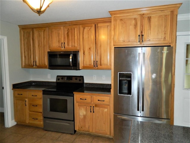 kitchen with stainless steel appliances, brown cabinetry, light tile patterned flooring, and dark countertops