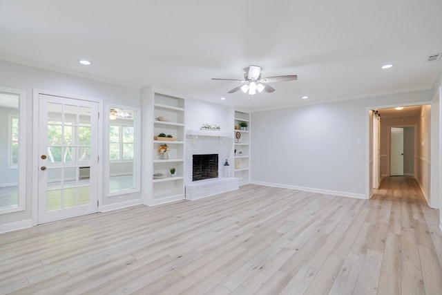 unfurnished living room featuring crown molding, ceiling fan, a brick fireplace, built in shelves, and light wood-type flooring