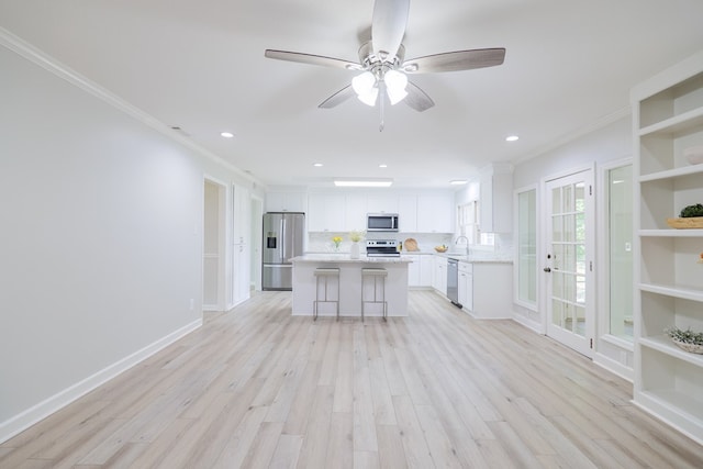 kitchen with a kitchen island, appliances with stainless steel finishes, white cabinets, ornamental molding, and light wood-type flooring