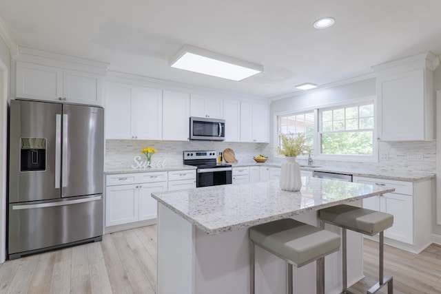 kitchen featuring a breakfast bar, white cabinetry, light stone counters, a kitchen island, and stainless steel appliances