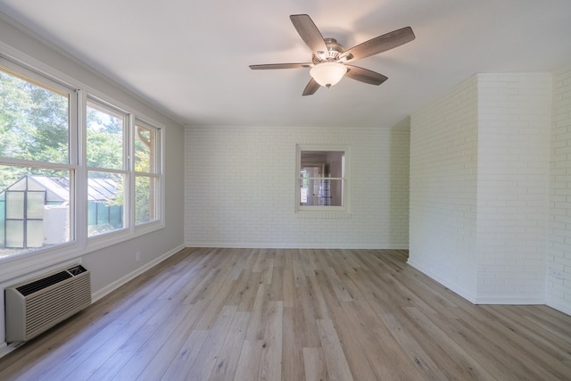 empty room with light hardwood / wood-style flooring, an AC wall unit, ceiling fan, and brick wall