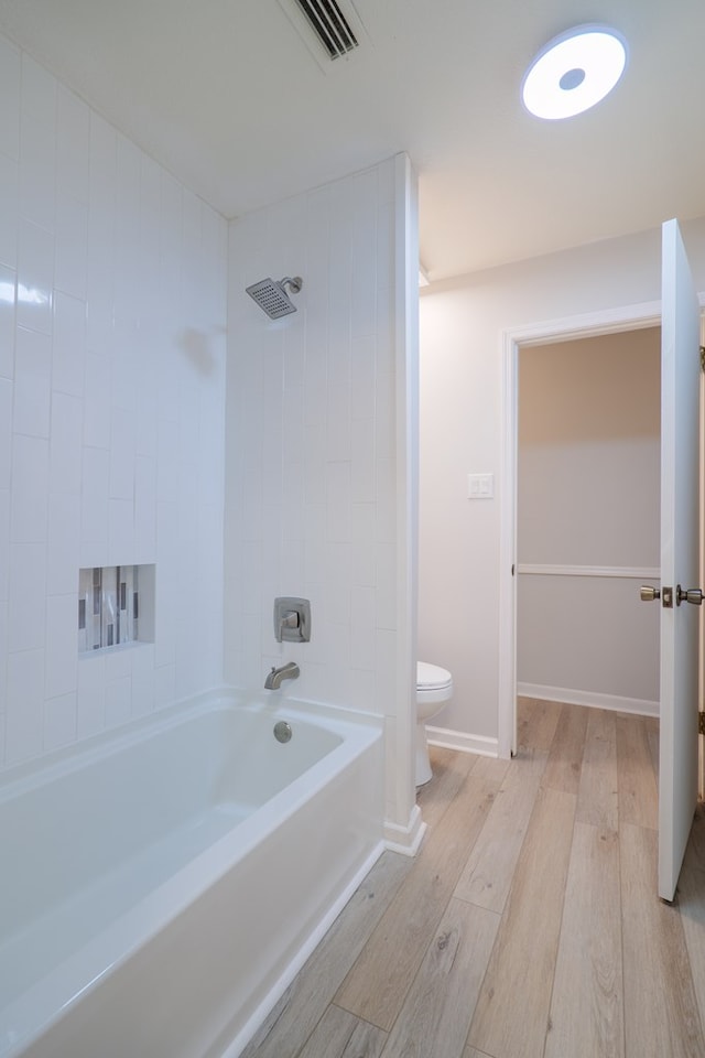 bathroom with hardwood / wood-style floors, tiled shower / bath, and toilet