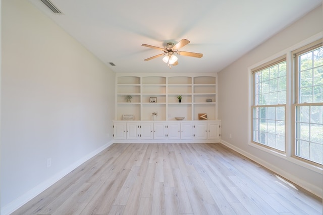 empty room with ceiling fan, built in features, and light wood-type flooring