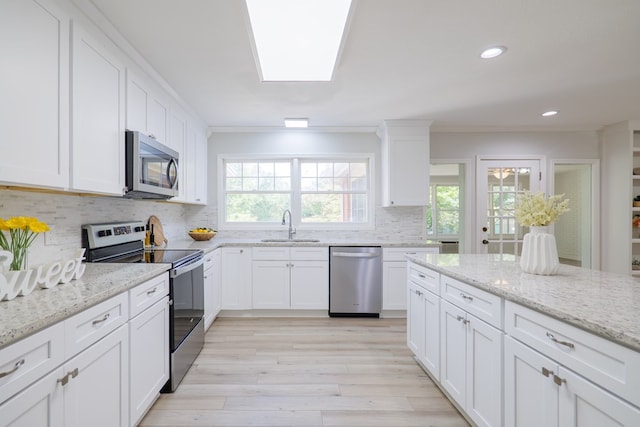 kitchen featuring sink, appliances with stainless steel finishes, white cabinetry, backsplash, and light stone countertops