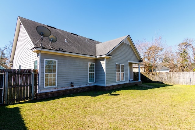 rear view of house with a yard, a shingled roof, and fence