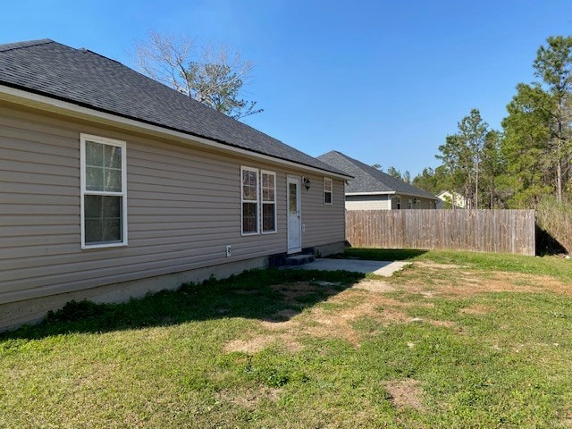 back of property with a yard, roof with shingles, and fence