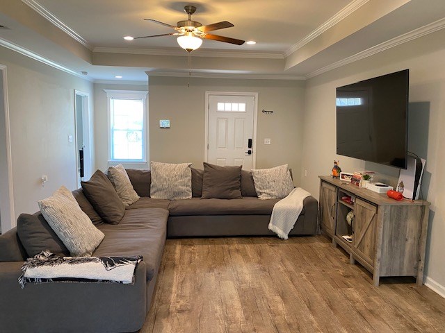 living area with light wood-style floors, recessed lighting, a raised ceiling, and crown molding