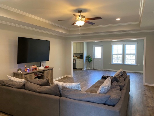 living room featuring baseboards, ceiling fan, wood finished floors, a tray ceiling, and crown molding