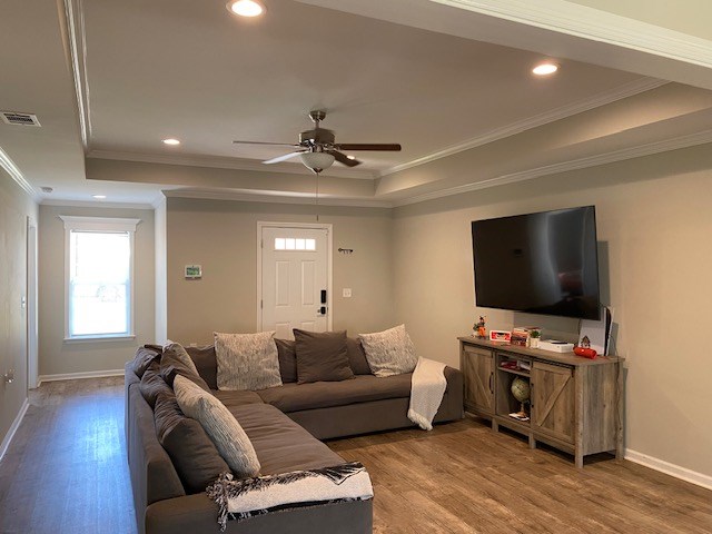 living area with a raised ceiling, visible vents, baseboards, and wood finished floors