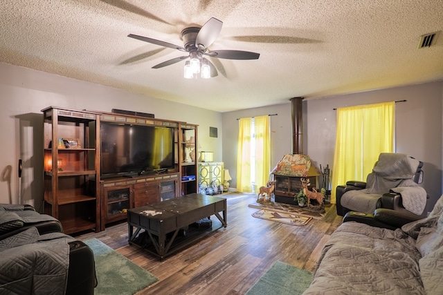 living room featuring hardwood / wood-style flooring, ceiling fan, a wood stove, and a textured ceiling