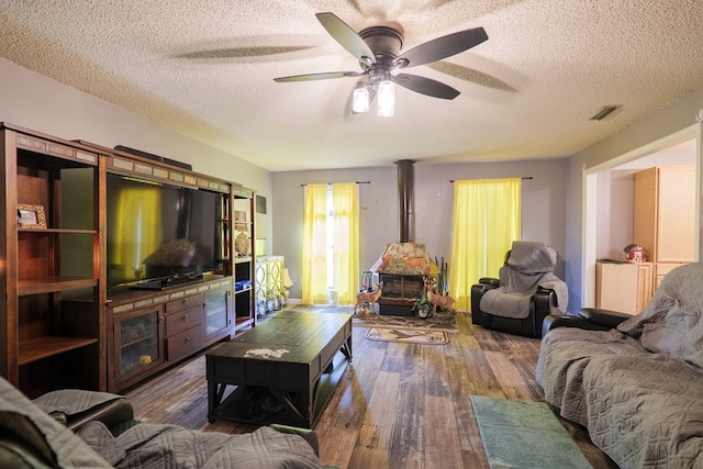 living room with ceiling fan, dark hardwood / wood-style flooring, a textured ceiling, and a wood stove