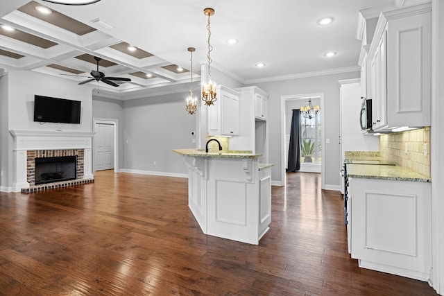 kitchen with tasteful backsplash, a brick fireplace, white cabinets, a peninsula, and ceiling fan with notable chandelier