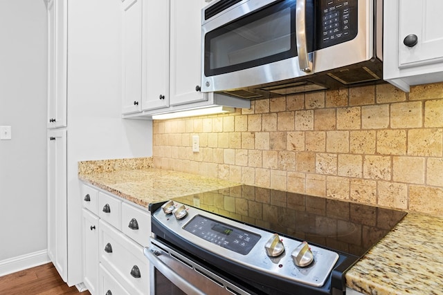 kitchen featuring stainless steel appliances, backsplash, white cabinetry, light stone countertops, and baseboards