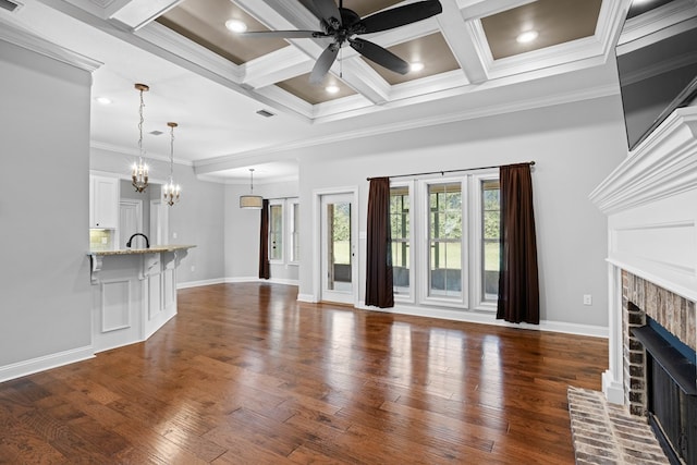 unfurnished living room featuring ceiling fan with notable chandelier, coffered ceiling, a fireplace, visible vents, and dark wood finished floors