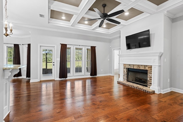 unfurnished living room with ceiling fan with notable chandelier, a fireplace, a towering ceiling, baseboards, and hardwood / wood-style floors