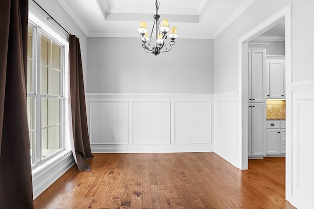 unfurnished dining area with a notable chandelier, crown molding, a raised ceiling, and wood finished floors