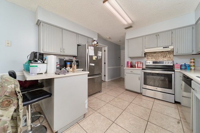 kitchen featuring stainless steel appliances, extractor fan, a textured ceiling, a kitchen bar, and light tile patterned floors