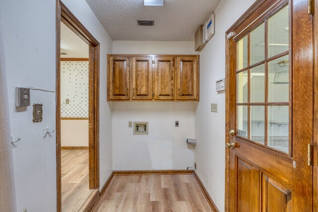 laundry area featuring washer and dryer, light wood-type flooring, a textured ceiling, and cabinets